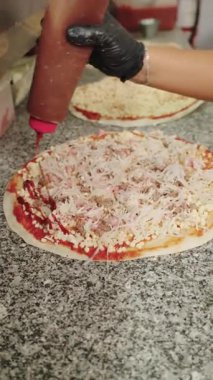 Profesyonel pizzacının barbekü sosunu peynir ve et malzemelerinin üzerine dökmesi. Ticari bir restoranın mutfağında İtalyan yemeği hazırlama