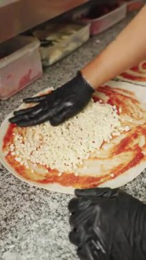 Siyah eldivenli profesyonel pizzaolo taze pizza hamuruna domates sosu üzerine dilimlenmiş mozzarella peyniri sürüyor.