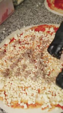 Profesyonel pizzacının siyah eldivenlerini takıp mozzarella peynirinin üstüne sosis ve domates sosunu çiğ hamur tabanı üzerine koyması.