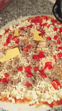 Siyah eldivenli profesyonel pizzacının üzerine fırında pişmemiş domates soslu, mozzarellalı ve etli sarı peynir parçaları koyması.