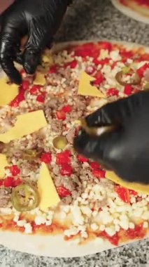 Profesyonel pizzacı siyah eldiven giyip Meksika usulü baharatlı pizzanın üzerine biber ve çedar peyniri serpiştiriyor.