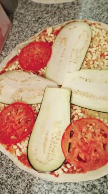 Profesyonel pizzacı dikkatli bir şekilde patlıcan ve domates dilimlerini vegan peynirli ve domates soslu bir pizzaya yerleştiriyor.