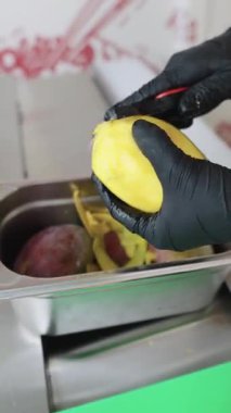İşçilerin elleri siyah nitril eldivenler içinde profesyonel bir mutfak ortamında sulu bir mangoyu soyarken ustalıkla yaklaş.