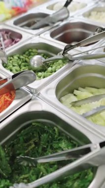 Paslanmaz çelik kaplarda çeşitli taze malzemelerin bulunduğu bir salata barını kapat. Restoranda ya da kafeteryada sağlıklı beslenme kavramı