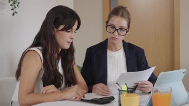 İki genç iş kadını bir sözleşmeyi gözden geçiriyorlar. Bir danışman bütçeyi açıklar ve kadın bir müşterinin giderlerini hesaplar