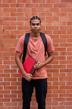 Saç stili ve sırt çantalı genç adam tuğla duvara yaslanmış, elinde kitap tutuyordu. Eğitim ve gençliği temsil etmek