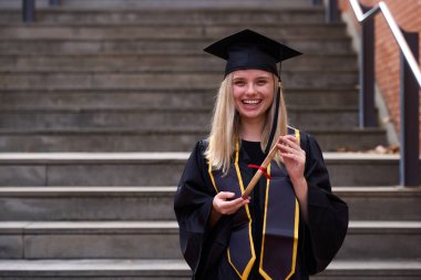 Mezuniyet şapkası ve cübbesi takan, diplomalı, akademik başarıyı ve başarıyı kutlayan genç bir kadın.
