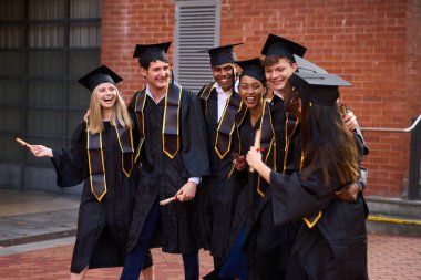 Bir grup mutlu genç üniversite mezunu başarılı bir akademik yılın ardından kucaklaşıyor, gülüyor ve diplomalarını gösteriyorlar.