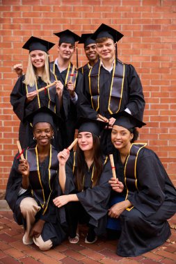 Çeşitli mutlu mezunlar akademik elbiseler giyip, gülümseyip, diploma taşıyarak, başarıyı ve parlak bir geleceği simgeleyen