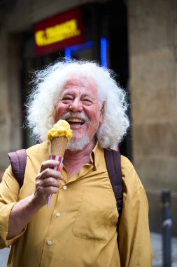 Beyaz saçlı, parlak gülümseyen, açık havada bir kepçe dondurma yiyen son sınıf öğrencisi.