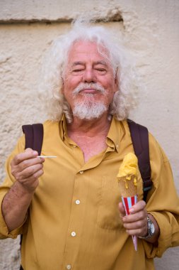 Beyaz saçlı ve sakallı son sınıf öğrencisi. Açık havada dondurma külahının tadını çıkarıyor. Gözleri kapalı, keyifle gülümsüyor.