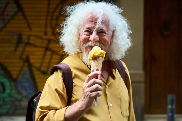 Mutlu son sınıf öğrencisi, beyaz saçlı, neşeli bir şekilde gülümseyen ve şehir caddesinde leziz bir dondurma külahı yiyen.