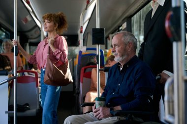 Tekerlekli sandalyedeki kıdemli bir adamla birlikte toplu taşıma araçlarında seyahat eden yolcular erişilebilirlik ve kapsayıcılığı vurguluyorlar.