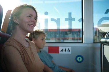 Güneşli bir günde gülümseyen anne ve oğlu toplu taşıma otobüsüne binip pencereden dışarı bakıyorlardı. Aile seyahati