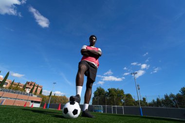 Kendine güvenen genç futbolcu. Ayağı futbol topunda güneşli bir günde antrenmana hazır.