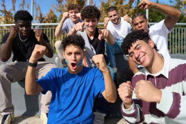 Bir grup farklı genç erkek arkadaş, açık hava etkinliğinde elde edilen başarıyı yumruklarıyla ve coşkulu ifadeleriyle kutluyor.