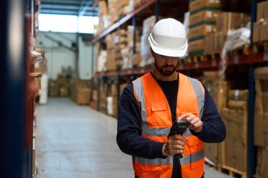 Warehouse worker in safety vest and hard hat scanning barcodes on boxes, managing inventory in a distribution center
