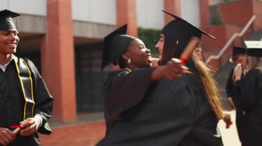 İki mutlu çok ırklı kadın mezun diplomalarını aldıktan sonra birbirlerine sarılıyorlar. Kampüsteki arkadaşlarla eğitim başarısını kutluyoruz.