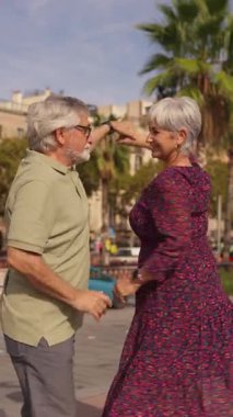 Gri saçlı, güneşli bir caddede salsa yapan neşeli emekli çift. Yaşlı adam ve kadın romantik bir anın tadını çıkarıyorlar.