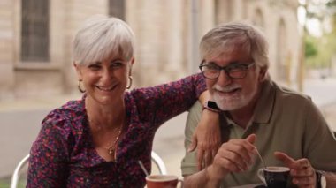 Açık bir kafede kahve molası verirken gülüp sohbet eden güzel bir çift. İki yaşlı arasında romantik ve neşeli bir an.