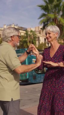 Güneşli bir günde halka açık bir meydanda gülümseyen ve dans eden olgun bir çift. Mutlu emekliler aktif bir yaşam tarzının keyfini çıkarıyorlar.