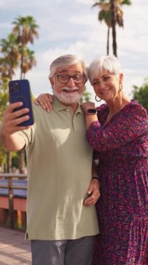 Tatildeki mutlu çift akıllı telefonuyla selfie çekiyor. Kadın erkeği kucaklarken gülümser ve birlikte komik suratlar yapar.