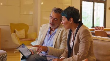 Ofis odasındaki bir kanepede oturan profesyonel erkek ve kadın. İş arkadaşları iş toplantısı yapıyorlar ve dijital tablet kullanıyorlar.