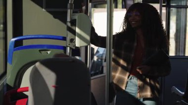 Kıvırcık saçlı neşeli genç bir kadın halka açık bir otobüste biletini onaylıyor. Modern ve sürdürülebilir ulaşım kullanılarak günlük ulaşım