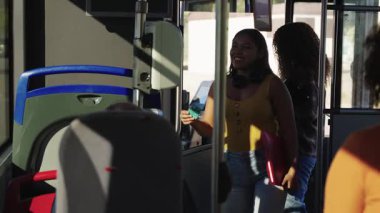 Otobüse binen ve biletlerini onaylayan iki gülümseyen bayan öğrenci. Genç bir kadın, yol parası için ulaşılamaz ödeme sistemini kullanır.
