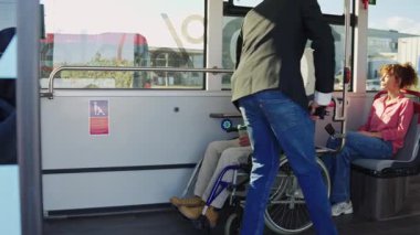 Merhametli genç adam, otobüste tekerlekli sandalyedeki yaşlı bir adama yardım ediyor. Üst düzey bir yolcuya toplu taşımada yardım eden gönüllü.