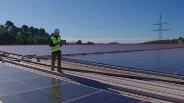 Kadın mühendis büyük bir güneş enerjisi santralini inceliyor. Fotovoltaik çiftliğin bakımı için bir tablet kullanan teknisyen