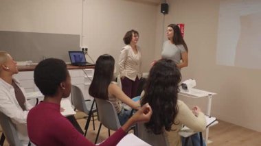 Çalışmalarını bir üniversite sınıfında sunan genç bir kadın. Profesör ve çeşitli bayan öğrenciler profesyonel bir eğitim sırasında dinliyorlar.