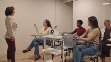 Genç bir kadın ders sırasında elini kaldırıyor ve bayan bir profesörle konuşuyor. Bir üniversite sınıfında dinleyen çeşitli öğrenci grupları