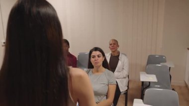 Sınıfta oturup sunum dinleyen bir grup insan. Çalışma kursuna ya da atölyeye katılan iş ekibi