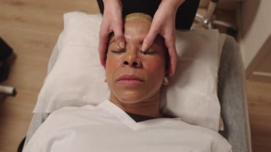 Rahatlamış bir kadın güzellik salonundaki profesyonel bir güzellik uzmanından canlandırıcı bir yüz masajı alıyor. Sağlık ve cilt bakımı kavramı