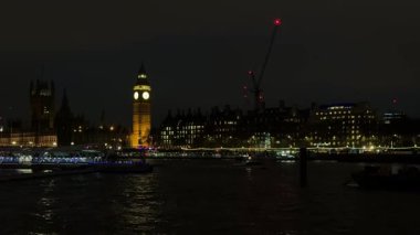 Londonlar ikonik gökyüzü geceleri parlıyor. Aydınlatılmış büyük Ben ve parlamento evleri, tekneler geçerken nehre yansıyor.