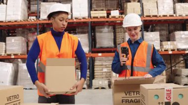 Siparişleri yerine getirmek için çalışan iki farklı kadın depo çalışanı. Bir kadın, meslektaşı bir paket hazırlarken bir barkod okuyucusuyla eşyaları tarıyor.