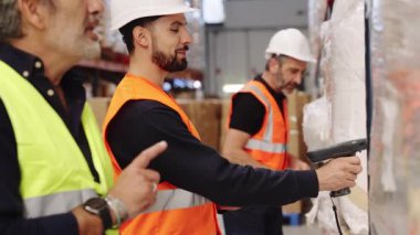 Depo çalışanları büyük bir dağıtım merkezinde envanter işletiyorlar. Meslektaşlar denetleme yaparken, bir çalışan paket üzerinde el tarayıcısı kullanır