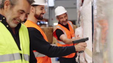 Dağıtım deposunda barkod tarayıcı kullanarak gülümseyen üç erkek işçi. Envanter ve lojistiği yöneten bir iş arkadaşı ekibi
