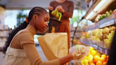 Young woman carefully choosing fresh green apples from the produce aisle in a modern supermarket. She is putting the fruit in a paper bag