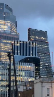 Finansal bir bölgede, akşam gökyüzüne karşı ışıldayan ofis pencereleri olan çağdaş cam gökdelenin ayrıntılı görüntüsü