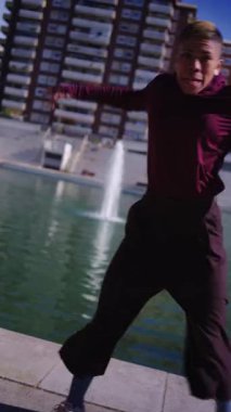 Parlak güneşli bir günde, şehir parkında modern saç stili dans eden modern dans figürleriyle etkileyici ve şık bir genç kadın.