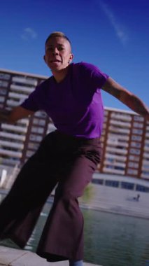 Çağdaş dans hareketleri yapan dövmeleri olan enerjik ve ikili olmayan biri. Güneşli bir şehir ortamında etkileyici serbest stil performansı