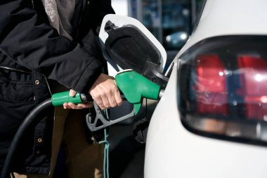 Yeşil yakıt hortumunu tutan kişi, benzin istasyonunda beyaz araba deposunu benzinle dolduruyor - fiyat artışı - benzin krizi