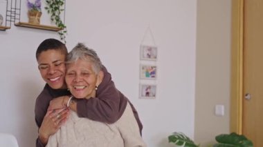 Sevgi dolu torun, neşeli yaşlı büyükannesini arkadan kucaklıyor. Nesiller arası sevgi ve aile bağları rahat bir yuva ortamında.