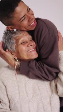 Sevecen bir torunla mutlu bir aile anı. Beyaz bir arka planda soyutlanmış sevgili büyük annesini şefkatle kucaklıyor ve öpüyor.