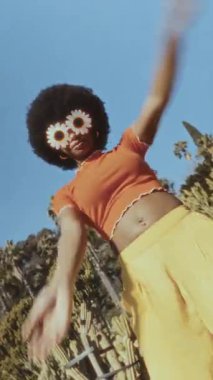 Dışarıda dans eden afro saçlı ve çiçek bardaklı modaya uygun Afro-Amerikan kadın. Eski moda görünüş eğlenceli ve tasasız bir yaşam tarzını kutluyor.