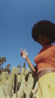 Afro saçlı, açık havada özgürce dans eden Afro-Amerikan bir kadının düşük açılı görüntüsü. Sıcak tonlar ve mavi gökyüzü ile klasik film görüntüsü