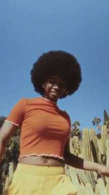 Afro saçlı, açık havada özgürce dans eden Afro-Amerikan genç ve mutlu bir kadın. Arka planda kaktüsleri ve palmiye ağaçları olan klasik film görüntüsü