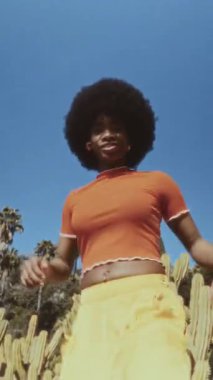 Açık havada afro saç stili dans eden güzel bir kadının düşük açılı çekimi. Bu klasik görüntüler onun neşeli enerjisini ve tarzını yakalıyor.